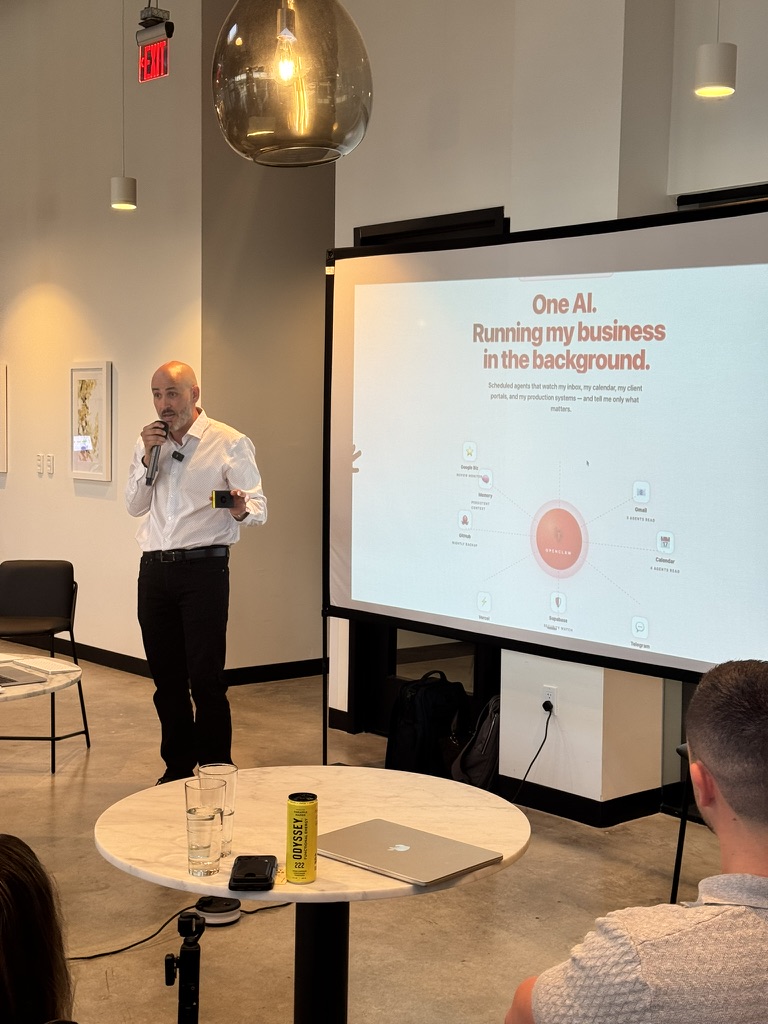 Antonio speaking beside a slide about one AI running business work in the background